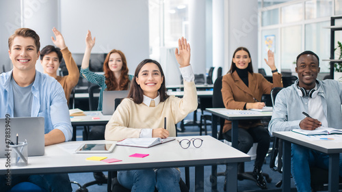 Portrait of diverse students raising hands at classroom © Prostock-studio