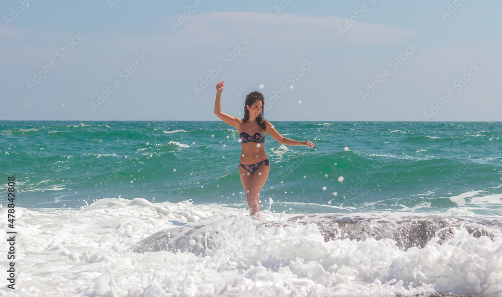 A beautiful emotional model girl splashes in the sea and laughs. Water splashes. Rest near the sea. The sea season.