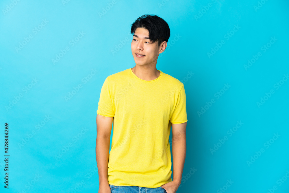 Young Chinese man isolated on blue background looking to the side and smiling Young Chinese man isolated on blue background looking to the side and smiling