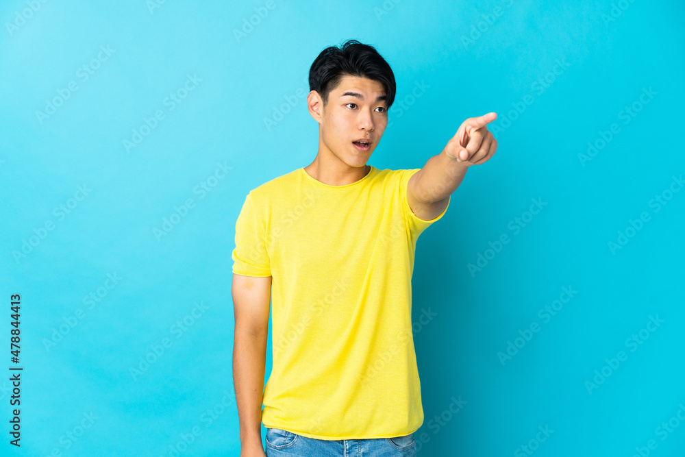 Young Chinese man isolated on blue background pointing away Young Chinese man isolated on blue background pointing away