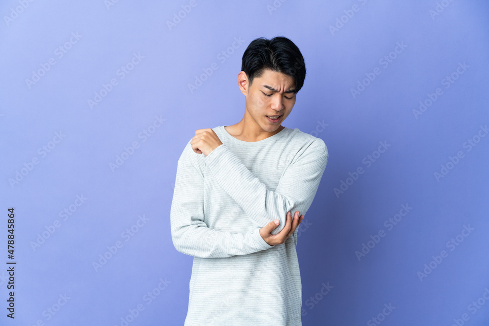 Young Chinese man isolated on purple background with pain in elbow Young Chinese man isolated on purple background with pain in elbow