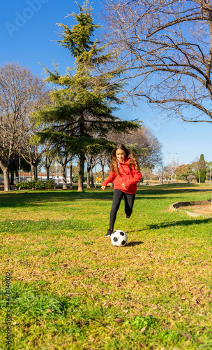 Pre-adolescent girl playing soccer in a park with natural grass. Exercise concept