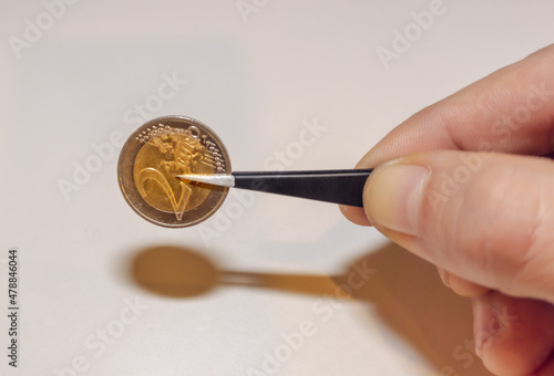 two euro coin in tweezers on a white background in a man's hand