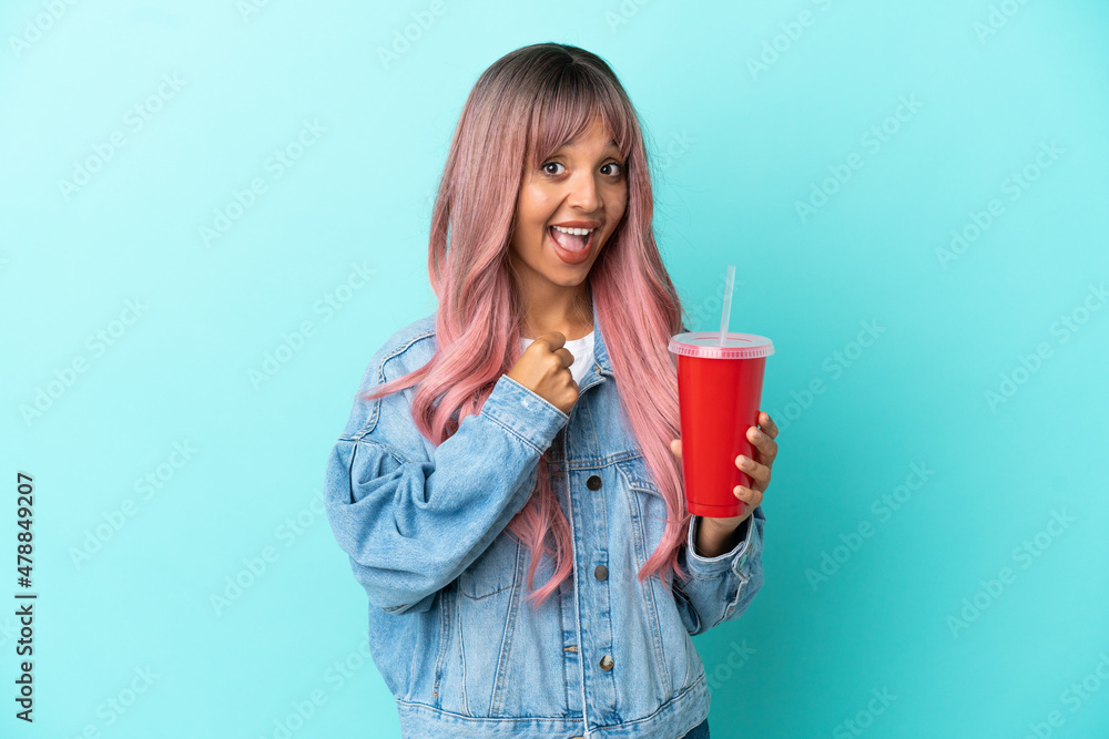 Young mixed race woman drinking a fresh drink isolated on blue background celebrating a victory Young mixed race woman drinking a fresh drink isolated on blue background celebrating a victory