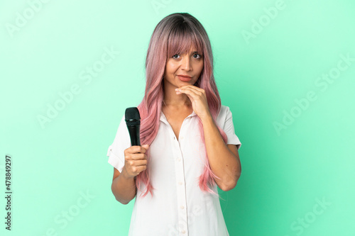 Young mixed race singer woman with pink hair isolated on green background thinking