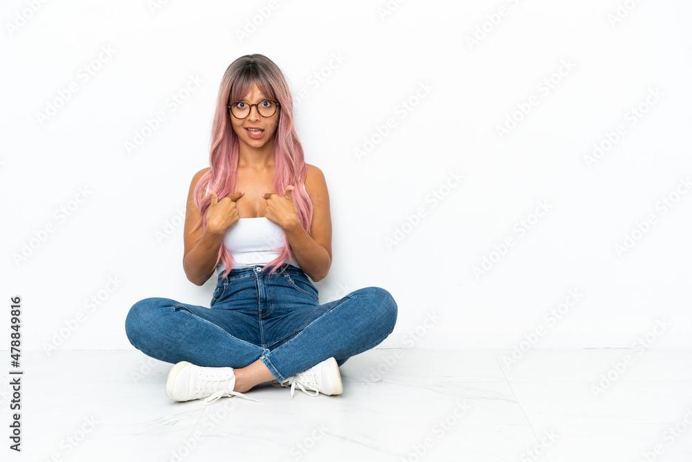 Young mixed race woman with pink hair sitting on the floor isolated on white background with surprise facial expression Young mixed race woman with pink hair sitting on the floor isolated on white background with surprise facial expression