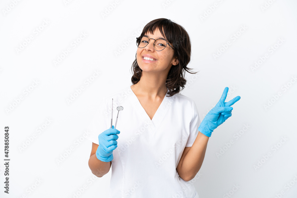 Young woman holding tools isolated on white background smiling and showing victory sign Young woman holding tools isolated on white background smiling and showing victory sign