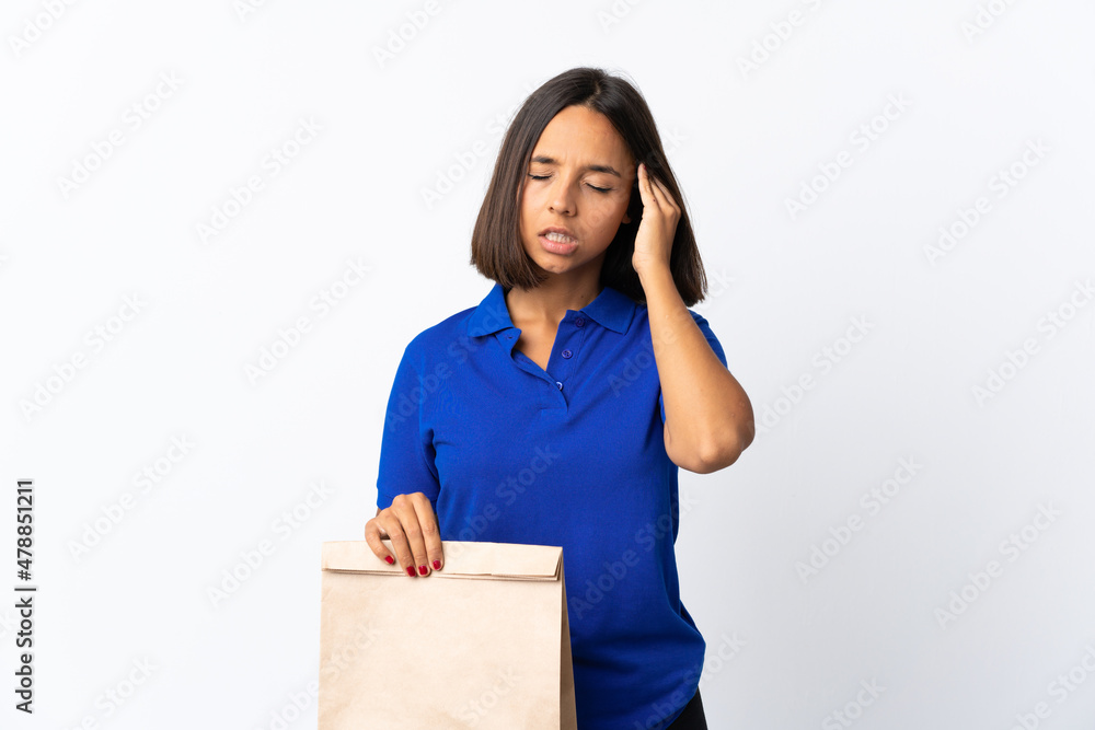 Young latin woman holding a grocery shopping bag isolated on white background with headache Young latin woman holding a grocery shopping bag isolated on white background with headache