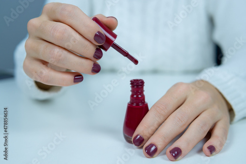 Young girl holding an open nail polish with one hand and the other holding the brush.