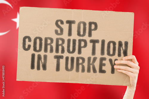 The phrase " Stop Corruption in Turkey " on a banner in men's hand with blurred Turkish flag on the background. Forbidden. Prevent. Wealth. Offence. Corruptness. Economy. Corruptible. Political