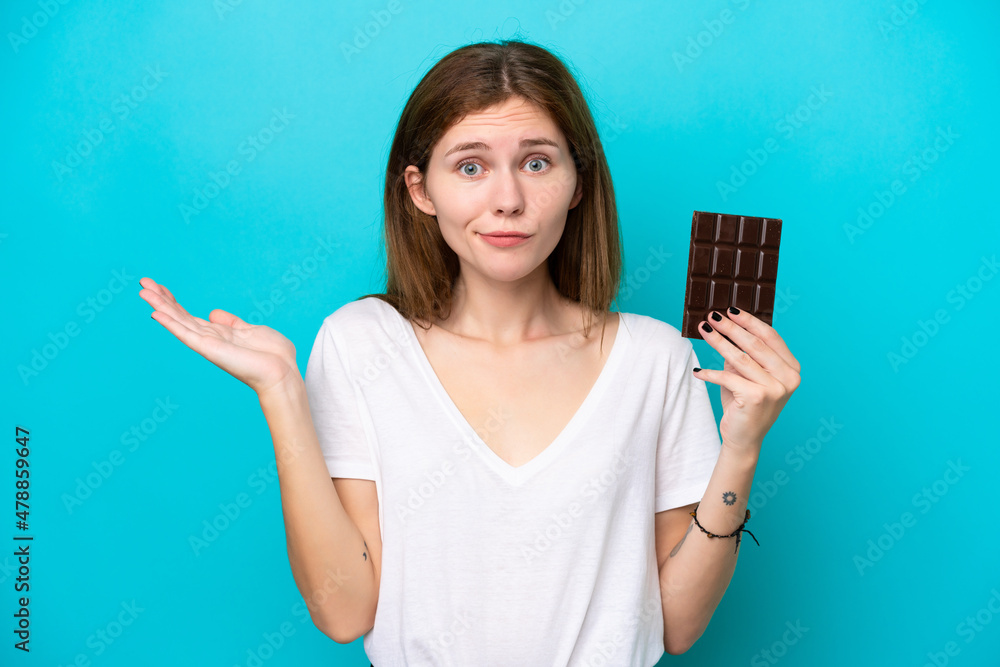 Young English woman with chocolat isolated on blue background having doubts while raising hands Young English woman with chocolat isolated on blue background having doubts while raising hands
