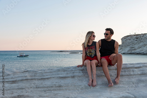 Couple sit on rocks by sea. They are looking into each other's eyes with love and passion.  Summer vacation. Relationship, valentine, romance, honey moon concept photo. Copy paste and text space. 