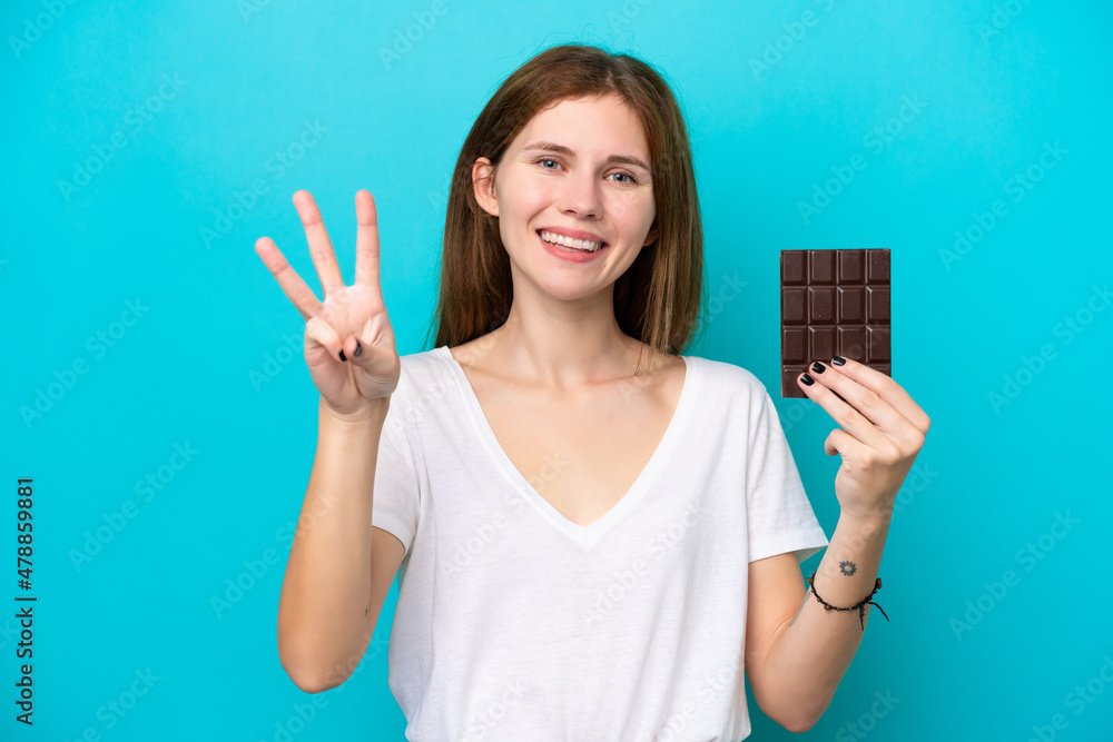 Young English woman with chocolat isolated on blue background happy and counting three with fingers Young English woman with chocolat isolated on blue background happy and counting three with fingers