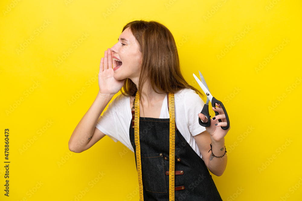 Young seamstress English woman isolated on yellow background shouting with mouth wide open to the side Young seamstress English woman isolated on yellow background shouting with mouth wide open to the side