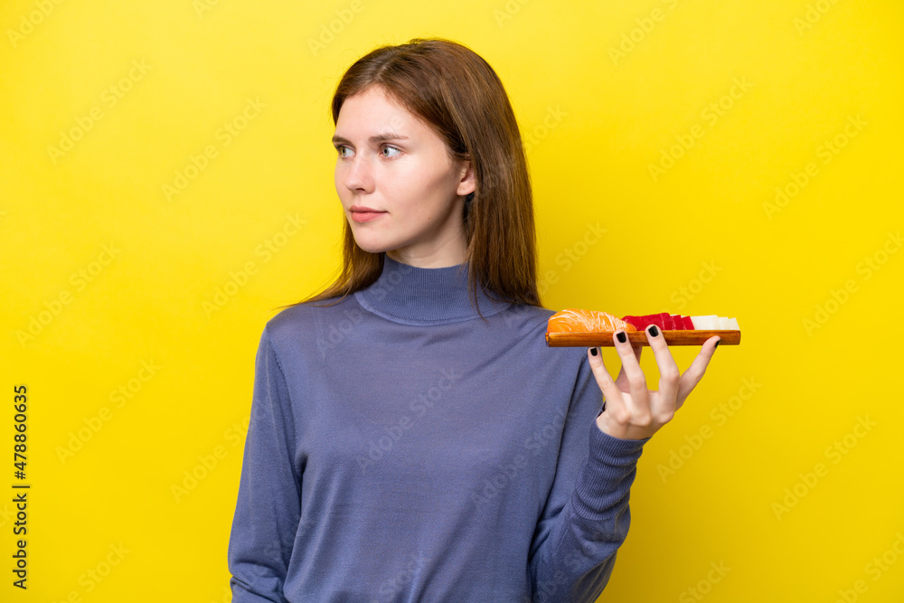Young English woman holding sashimi isolated on yellow background looking to the side Young English woman holding sashimi isolated on yellow background looking to the side