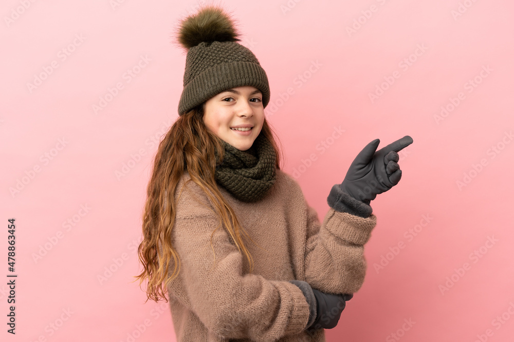Little girl with winter hat isolated on pink background pointing finger to the side Little girl with winter hat isolated on pink background pointing finger to the side