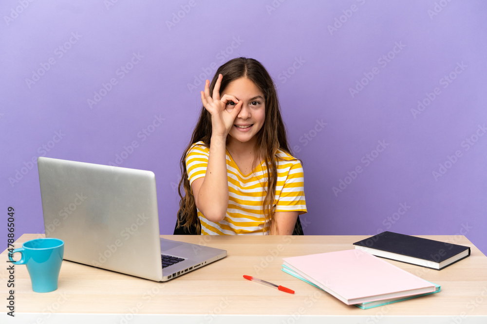 Little student girl in a workplace with a laptop isolated on purple background showing ok sign with fingers Little student girl in a workplace with a laptop isolated on purple background showing ok sign with fingers
