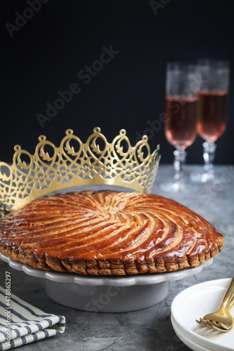 A traditional French galette des rois or king cake on a plate with crown and glasses of apple cider in background. Cake made with puff pastry and creamy almond filling roll in a circle shape photo