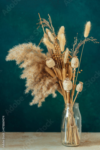 Fototapeta Bouquet of beige dried flowers in a glass vase on green blue background