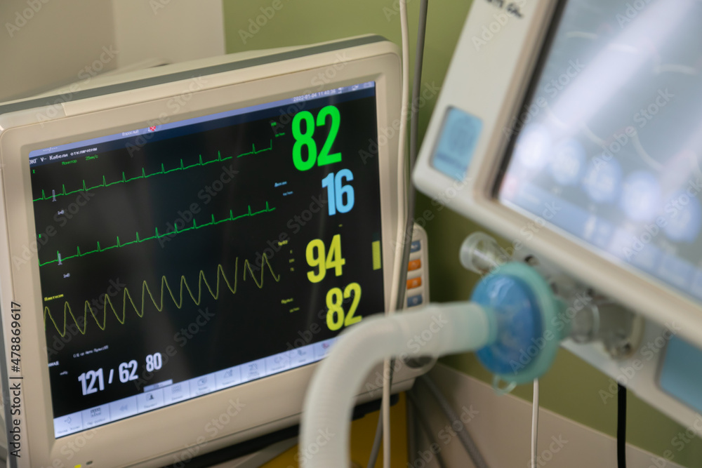 Fototapeta premium A bedside patient monitor surrounded by medical equipment of an intensive care unit. The screen is on and brightly shows patient parameters: oxygen saturation, ekg, blood pressure.