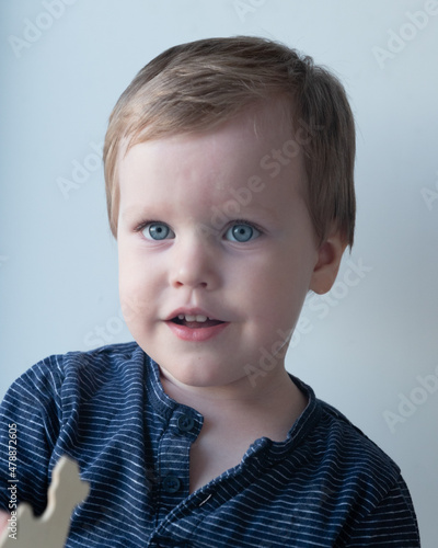 portrait of a little boy with blue eyes in a blue blouse on a white background smiling