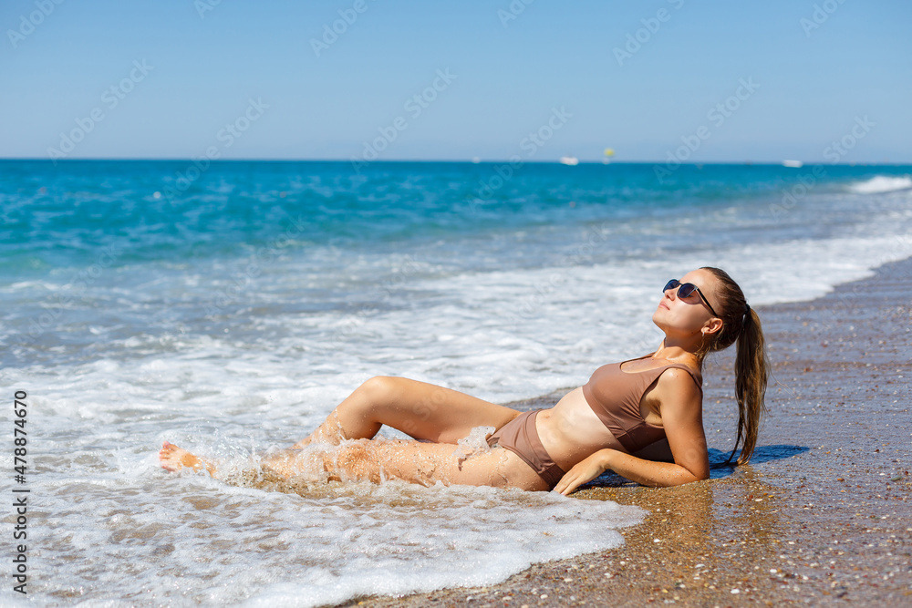 An attractive young woman in a bikini lies on the sand by the sea, relaxing on a deserted beach. Beautiful model in a swimsuit resting on the fine sand on a tropical island An attractive young woman in a bikini lies on the sand by the sea, relaxing on a deserted beach. Beautiful model in a swimsuit resting on the fine sand on a tropical island