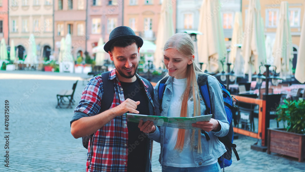 Fototapeta premium Zoom shot of tourists holding map and smiling to the camera. They standing on a big market square of old european city.