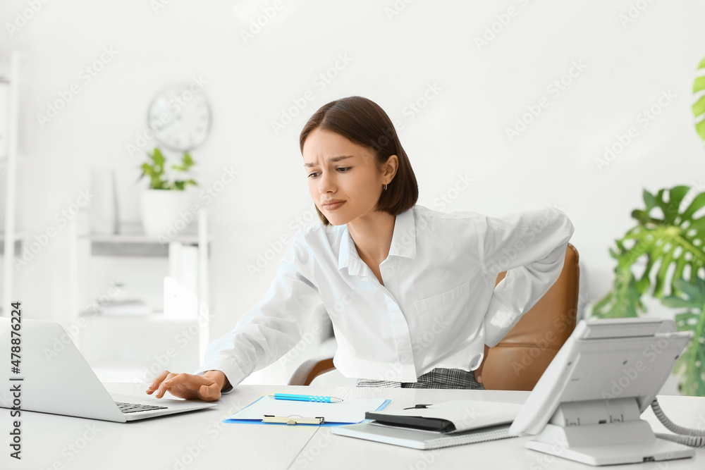 Young woman feeling back pain in office Young woman feeling back pain in office