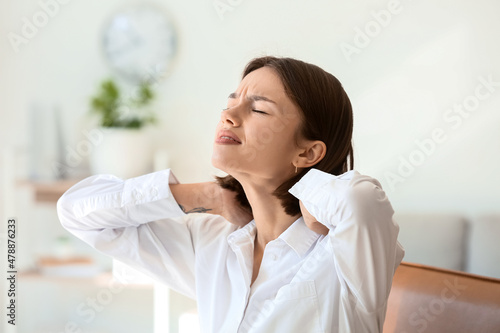 Young woman feeling neck pain in office