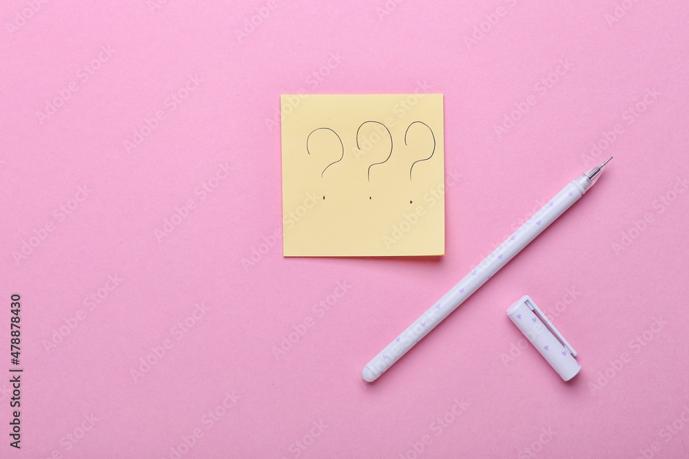 Sticky note with question marks and pen on pink background Sticky note with question marks and pen on pink background