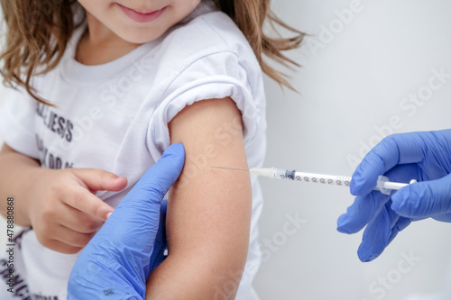Criança tomando vacina no braço com prevenção do covid 19 e medico com luva azul e seringa na mão. photo