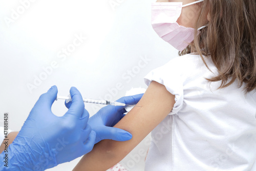 Criança tomando vacina no braço com prevenção do covid 19 e medico com luva azul e seringa na mão.
