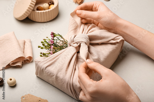 Woman wrapping gift box in fabric on light background, closeup photo