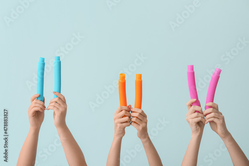 Hands with popular pop tubes on color background