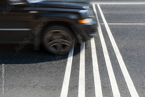 Rumble strips or speed breakers on asphalt road surface and black car crossing them in motion blur. Traffic calming concept.