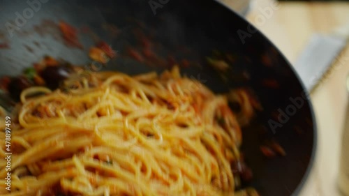Tossing spaghetti in a pan with sauce, pasta puttanesca