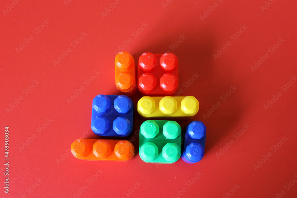 Pieces of plastic rainbow multicolored buildable toy blocks formed and arranged on red background Pieces of plastic rainbow multicolored buildable toy blocks formed and arranged on red background