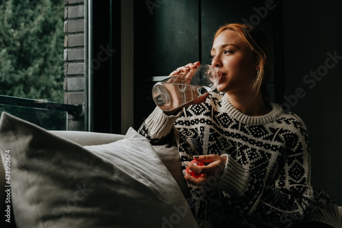woman drinking water looking out the window at home