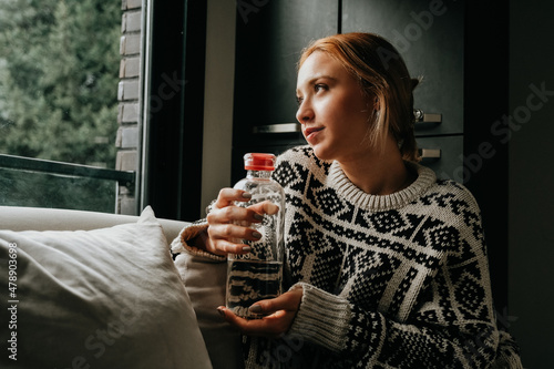 woman drinking water looking out the window at home