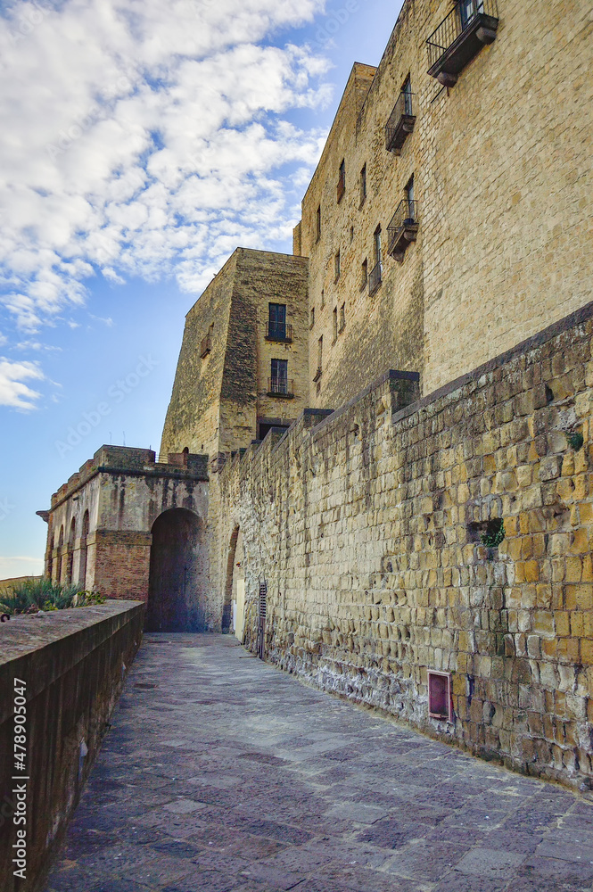Blue sky with clouds, paved passage and outer walls of the Castel dell'Ovo (Egg Castle), a seafront castle in Naples, on the island of Megaride, on the Gulf of Naples in Campania, Italy.