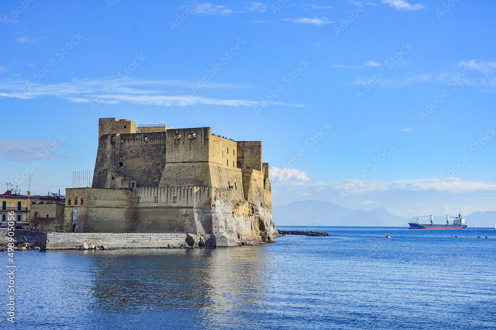 Cargo ship and sea view with Castel dell'Ovo (Egg Castle), a seafront castle in Naples, on the former island (now a peninsula) of Megaride, on the Gulf of Naples in Campania, Italy.