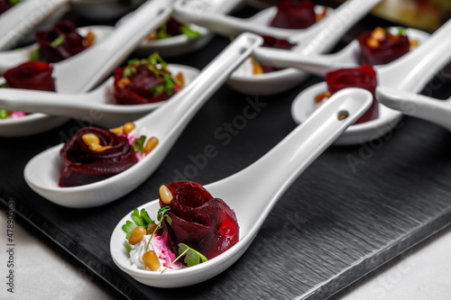 A light snack of beetroot, whipped cream, pine nuts and herbs in a dessert spoon is on the table.