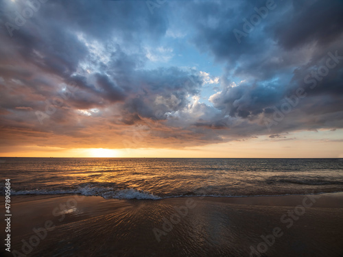 Beautiful sunset over the calm sea with cloud sky background. Sunset over tropical beach. Nature summer  concept. Peak sunset over sea with yellow light reflect on sea water. Tranquil seascape. © AKGK Studio