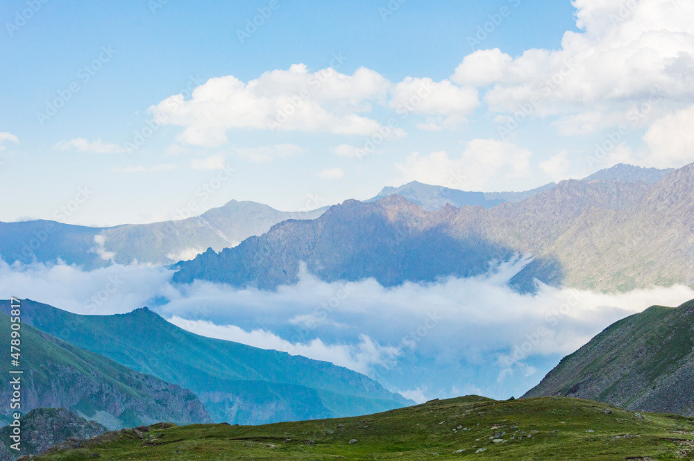 Fototapeta premium Caucasian mountains in Kazbegi national park in Georgia, blue sky with clouds, rocks, stones, fog in canyons, green grass