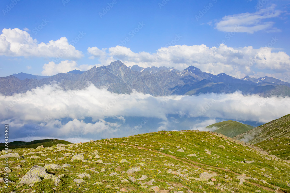 Caucasian mountains in Kazbegi national park in Georgia, blue sky with clouds, rocks, stones, fog in canyons, green grass
