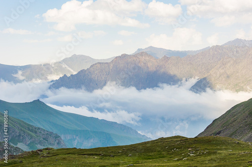 Caucasian mountains in Kazbegi national park in Georgia, blue sky with clouds, rocks, stones, fog in canyons, green grass photo