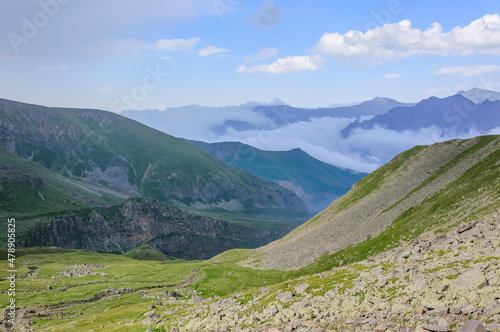 Caucasian mountains in Kazbegi national park in Georgia, blue sky with clouds, rocks, stones, fog in canyons, green grass