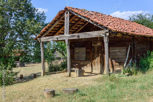 Traditional georgian house in Tbilisi open-air ethnographical museum. Wooden walls, tiled roof, dry grass, green trees and bushes, blue sky