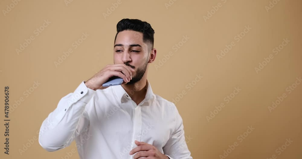 Businessman holding mobile phone while singing and dancing over beige background Businessman holding mobile phone while singing and dancing over beige background