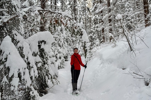 Woman in red sport jacket snowshoeing in winter forest covered with fresh snow. Canadian Rokies. Banff National park.  Alberta. Canada photo